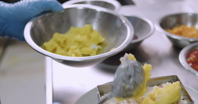 hands wearing blue gloves putting a layer of mashed potato during the preparation of Peruvian Causa