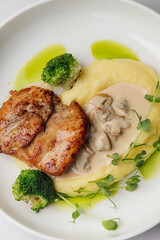 Grilled chicken breast is served with creamy mashed potatoes, steamed broccoli florets, fresh pea shoots, and a rich mushroom sauce. Restaurant or cafe menu, cookbook recipe