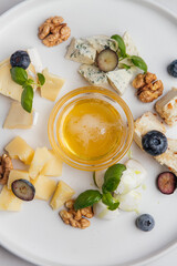 Round white plate with assorted cheese, honey, blueberries, walnuts and basil leaves, arranged in a beautiful composition, creating food presentation. Restaurant or cafe menu, cookbook recipe
