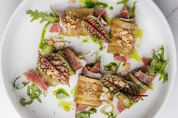 Grilled zucchini rolls, filled with prosciutto and chopped nuts, are artfully arranged on a white...