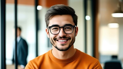 Fototapeta premium Portrait, young man, glasses, bright orange sweater, confident smile, white teeth, short dark hair, styled haircut, office hallway background, professional environment, warm lighting, shallow depth of