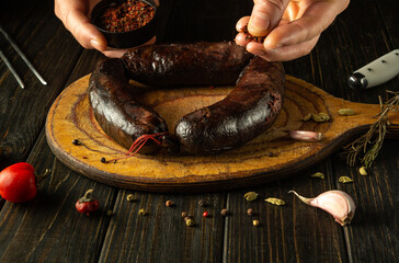 Adding dry spices by hand to blood sausage for flavor and aroma. On a wooden board black sausage...
