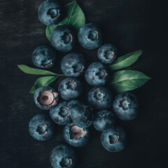 Fresh blueberries with leaves on dark wooden background. Concept of healthy eating, antioxidants, and summer harvest.