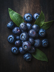 Fresh blueberries with leaves on dark wooden background. Concept of healthy eating, summer fruits, and antioxidants.