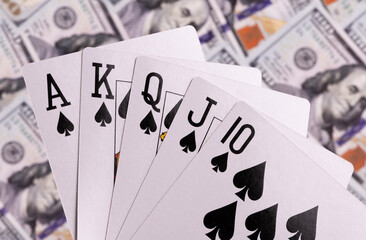 Royal flush of spades, the strongest hand in poker, against a background of $100 bills