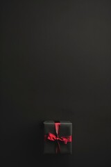 Striped and red gift box with black ribbon on textured dark surface