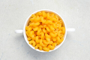 White ceramic bowl of raw pasta. Top view. On a light stone background.