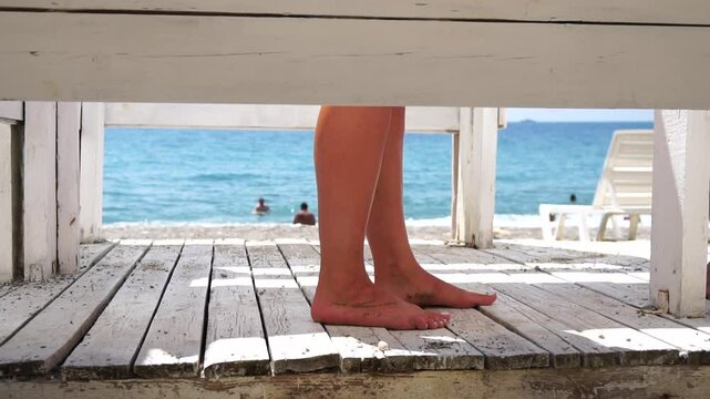 Woman in the changing, dressing room on beach, at sunset on the seashore. Close-up of bare female feet legs in enclosed changing room cabin. Summer holiday vacation and travel concept. Slow motion