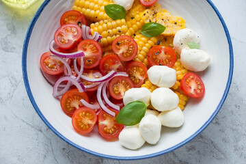 Salad with corn, red cherry tomatoes and mozzarella cheese served in a blue and white plate, horizontal shot, middle close-up