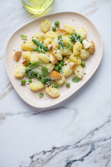 Potato gnocchi with cheese, green peas, beans and basil, vertical shot on a white stone background with space, high angle view