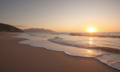 Obraz premium A tranquil beach scene at sunset, with the sky reflecting a mocha mousse hue as the sun sets over