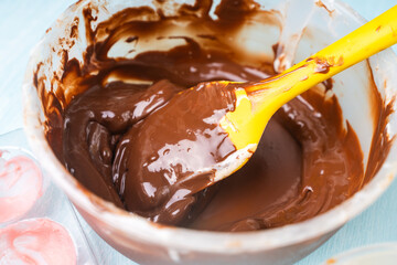 Tempering dark professional chocolate. The process of making handmade chocolates. Bowl with melted chocolate and yellow spatula on blue background