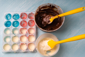 The process of making handmade chocolates. A candy mold with colorful dyes and bowls with white and dark chocolate.