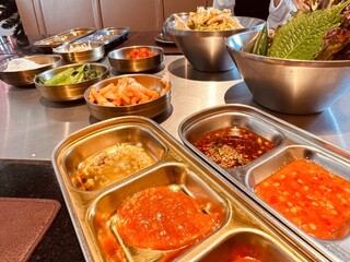 A vibrant assortment of Korean side dishes, including kimchi and sauces, displayed on a metal table for a traditional meal.