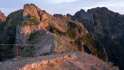 Hiking trail with mountains in backdrop catching soft orange light during sunrise, Madeira, Portugal