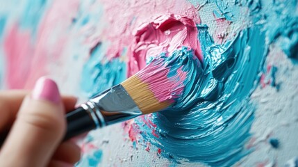 Fototapeta premium A hand holding a brush applies blue and pink paint on a canvas. The artistic act of painting is captured, highlighting creativity and the blending of colors.