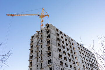 Fototapeta premium Tower cranes next to a multistory panel building under construction in the city against a blue sky.