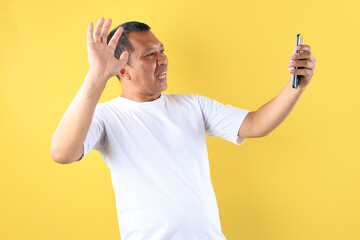 Middle Age Old asian Man Wearing White tshirt Holding Mobile Phone and using it to Video Call