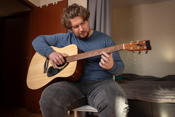 Obraz premium Man Practicing Guitar in Cozy Bedroom, individual engaged in musical study, learning instrument basics in leisure time.