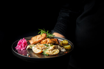 A beautifully plated dish featuring succulent meat, creamy sauce, pickled vegetables, and fresh herbs, served on a stylish black plate. Perfect for culinary highlights or gourmet menus.
