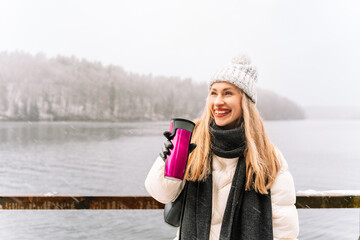 cheerful woman holding a thermos cup near a snowy lake