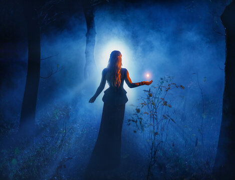 art photo real person beautiful fantasy woman holding magic light in hands, glowing ball fly in air illuminates way in dark night forest fog tree. Girl elf magician sexy dress. mystic lady sorceress