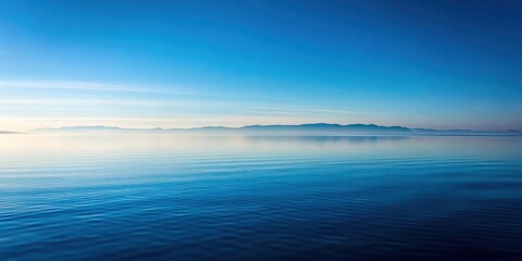 Serene waters reflecting a distant mountain range under a clear, azure sky