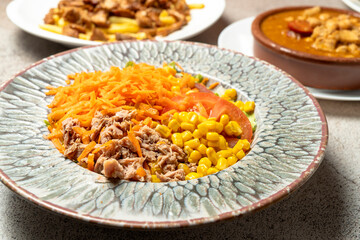 Tuna salad with grated carrots, corn kernels, tomato slices and lettuce in a rustic ceramic plate, part of a healthy meal