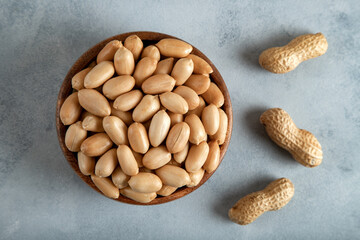 Bowl of shell and roasted peeled peanuts on dark background, top view
