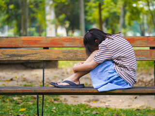 A sad little girl is sitting alone on bench in park. The little girl is unhappy and anxious because...