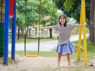 Cute girl having fun on the swing in the playground in the park. Children playing in the playground during summer vacation.