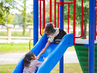 Fototapeta premium Cute sisters having fun on a colorful slide in an outdoor park. Children playing in the playground during summer vacation.