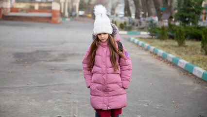 Fototapeta premium Child girl wearing winter clothes with backpack outdoors go to school