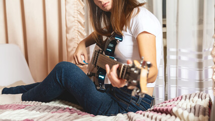 Side view of young brunette woman playing guitar on bed at home