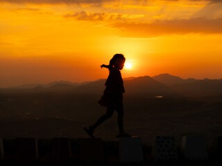 Silhouette of cute little girl playing happily on summer sunset background.