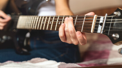 Fototapeta premium Close-up of a women playing a guitar on a bed. Guitar strings visible. Relaxed atmosphere with an emphasis on music. A woman plays an electric guitar.