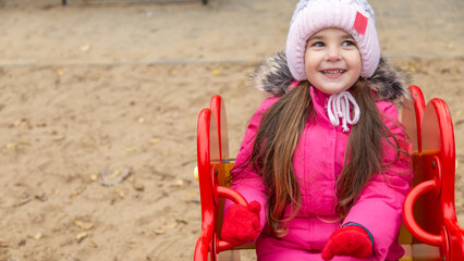 Little girl having fun on playground. Happy healthy little child climbing, swinging and sliding on different equipment. Child on cold day in colorful clothes outdoors