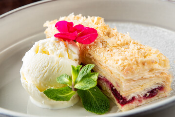 A delicious dessert featuring a flaky pastry layered with berry filling, complemented by a scoop of vanilla ice cream and garnished with mint leaves and edible flowers.