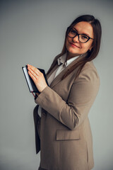 Confident businesswoman wearing a beige suit and eyeglasses, holding a closed notebook while...