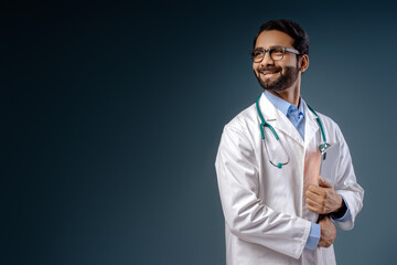 Smiling, happy, professional Indian man, doctor, wearing white coat, stethoscope, holding laptop