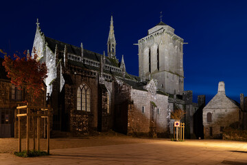 Obraz premium L'église de Locronan la nuit, éclairée par quelques réverbères. Le ciel bleu de l'heure bleue enveloppe l'ensemble, créant une ambiance sereine et mystérieuse.