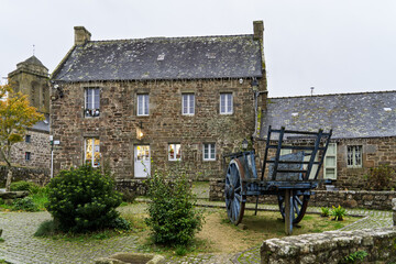 Une petite place de Locronan, où une charrette en bois repose tranquillement, entourée de maisons...