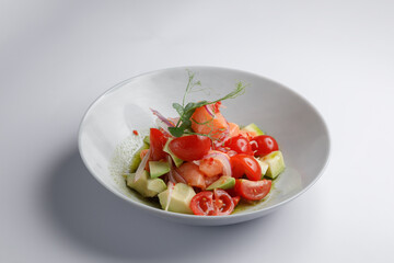 A salad with tomatoes, avocado, and cucumber in a white bowl