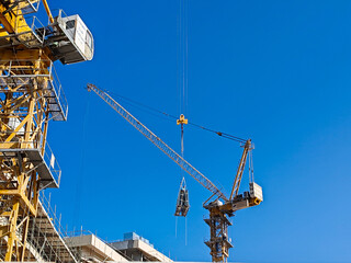 Naklejka premium Tower crane or mobile crane erected beside under construction building. Yellow color tower crane or Mobile crane used for lifting heavy items or materials from ground to top level for high buildings. 