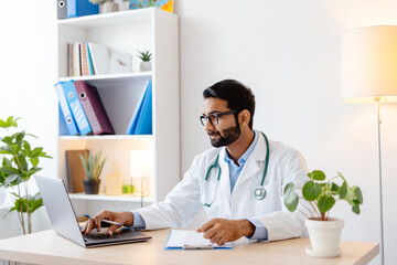 Pensive, Indian man, professional doctor wearing white coat, stylish eyeglasses using laptop