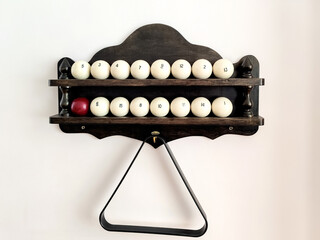 Billiard balls and triangle for pyramid are on wooden shelf attached to light colored wall. Copy...