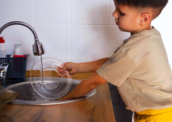 Funny 5 yearold boy is washing dishes standing at the sink. Housework assistant, the concept of work.