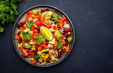 Mexican style salad with tuna, avocado, corn, beans, tomatoes and cilantro, black background, top view