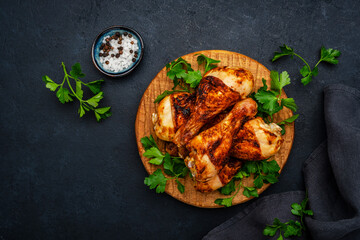 Baked chicken legs or drumsticks in spices on wooden serving board, black background, top view
