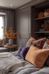 Cozy bedroom with grey bedding, orange and purple pillows, and built-in shelving.